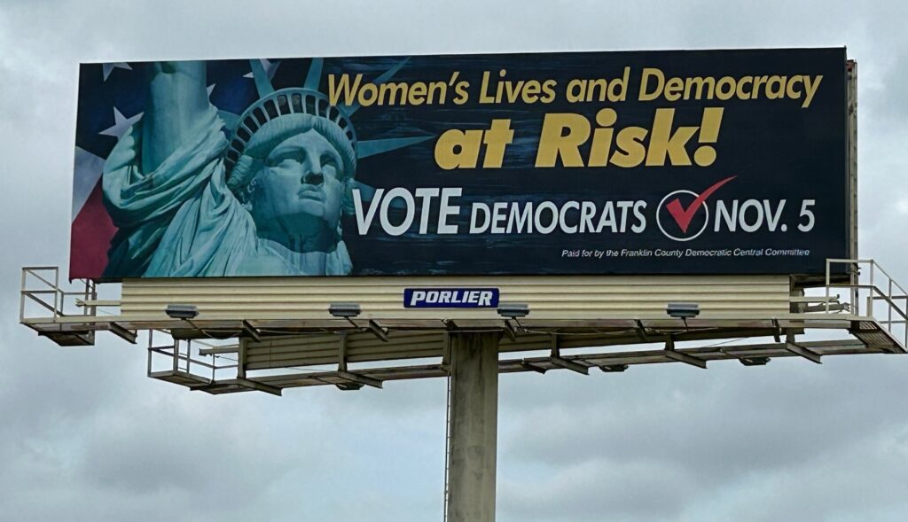 Picture of a billboard with the words "Women's Lives and Democracy at Risk! Vote Democrats!